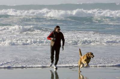 PACIFIC GROVE, CA - FEBRUARY 07:  A woman runs with her dog along the beach February 7, 2006 in Pacific Grove, California. The U.S. saw its warmest January on record with a national average of 39.5 degrees Fahrenheit, beating the old record for January temperatures of 37.3 degrees set in 1953. Due to the unseasonably warm weather, Americans have been able to save on heating bills just as oil prices have hit record highs. Temperatures in the Monterey Bay are expected to in the 70's with clear skies for the next five days.  (Photo by Justin Sullivan/Getty Images)