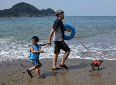 TOYOOKA, JAPAN - AUGUST 23: A man walks with his son and pet dog take a bath in the sea at Takeno Beach on August 23, 2014 in Toyooka, Japan. This beach is open for dogs and their owners every summer between the months of June and September. (Photo by Buddhika Weerasinghe/Getty Images)