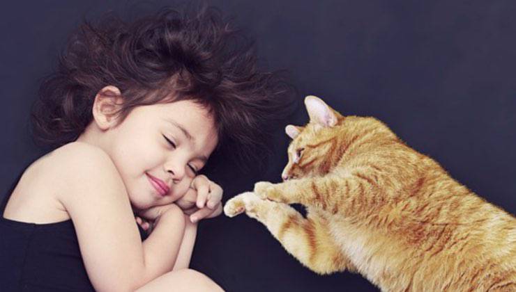 Bambina sdraiata accanto a un gatto arancione 