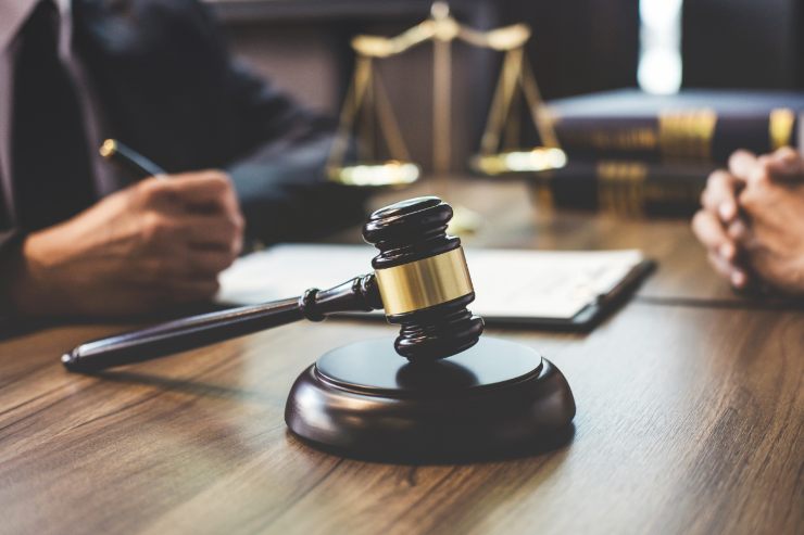 Un giudice che compila dei documenti che ha sulla scrivania insieme al martello da giudice e la bilancia di giustizia